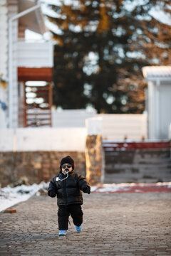 Joyful curious and independent toddler kid walks along the path in the winter forest. A little boy in warm overalls and a hat enjoys a walk in the winter snowy forest during winter holidays.