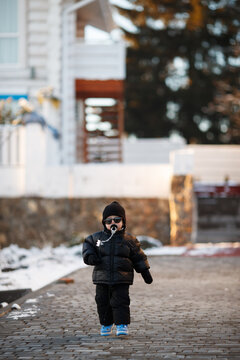 Joyful curious and independent toddler kid walks along the path in the winter forest. A little boy in warm overalls and a hat enjoys a walk in the winter snowy forest during winter holidays.