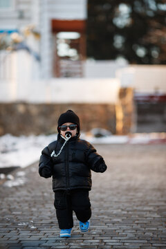 Joyful curious and independent toddler kid walks along the path in the winter forest. A little boy in warm overalls and a hat enjoys a walk in the winter snowy forest during winter holidays.