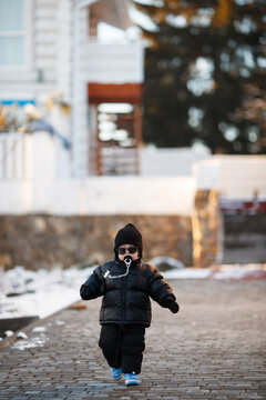 Joyful curious and independent toddler kid walks along the path in the winter forest. A little boy in warm overalls and a hat enjoys a walk in the winter snowy forest during winter holidays.