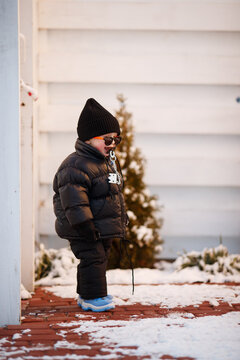 Joyful curious and independent toddler kid walks along the path in the winter forest. A little boy in warm overalls and a hat enjoys a walk in the winter snowy forest during winter holidays.