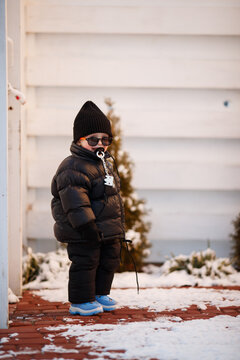 Joyful curious and independent toddler kid walks along the path in the winter forest. A little boy in warm overalls and a hat enjoys a walk in the winter snowy forest during winter holidays.