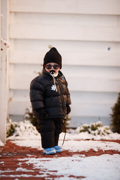 Joyful curious and independent toddler kid walks along the path in the winter forest. A little boy in warm overalls and a hat enjoys a walk in the winter snowy forest during winter holidays.