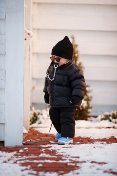 Joyful curious and independent toddler kid walks along the path in the winter forest. A little boy in warm overalls and a hat enjoys a walk in the winter snowy forest during winter holidays.
