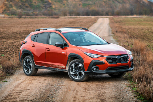 Brno, Czech Republic - February 15, 2025: Orange Subaru Crosstrek crossover stands outdoors in nature on a dirt road. Modern Japanese hybrid car.