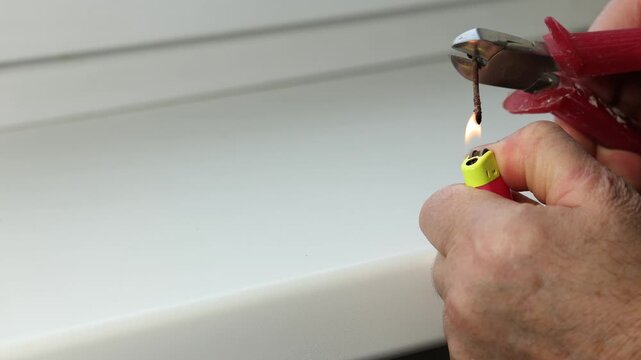 A specialist heats a rusty nail with a lighter for work.