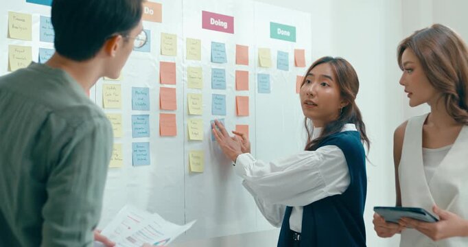 Group of Asian businesspeople work together collaborating and sharing ideas use colorful note on wall in business meeting in office. Financial generation z team brainstorm on e-Commerce project.