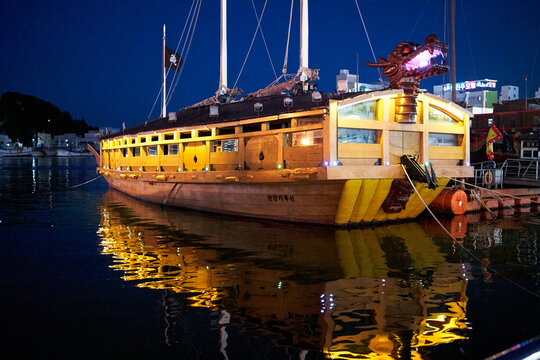 A life-size reconstruction of a historic Joseon-era Geobukseon (Turtle Ship) illuminated at night in the calm waters of Gangguan Port, Tongyeong, South Korea, featuring its distinctive dragon head