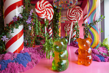 Giant green and orange gummy bears with red and white lollipops in a whimsical candy land scene with pink textures