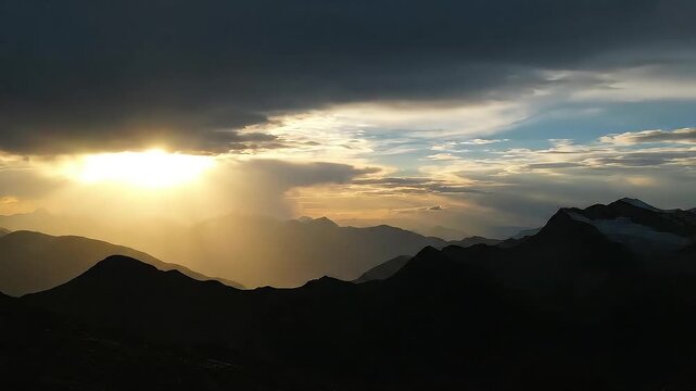 Golden sunbeams break through dramatic clouds over silhouetted mountain ranges.