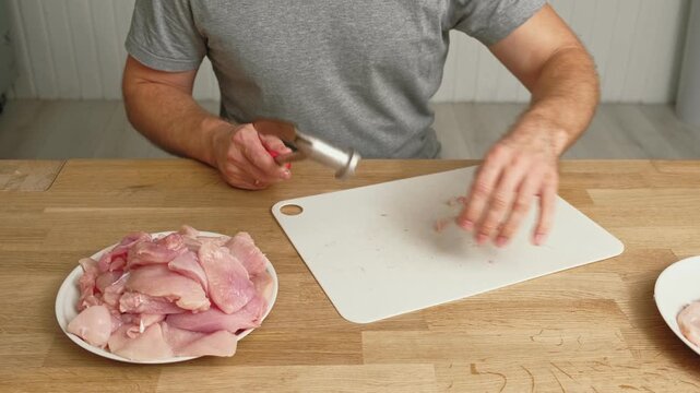 Person using meat tenderizer on raw chicken. Chef preparing pork loin slice with meat mallet on cutting board. Man tenderizing fillet. Cooking cutlets pounding poultry breast close-up. Culinary dish.