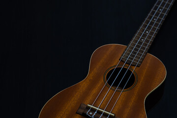 Fototapeta premium Close up of a brown wooden classic Hawaiian ukulele body and strings on a dark background.