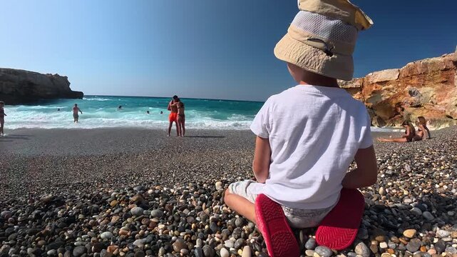Little boy are sitting on the Cretan beach with stormy sea, Spilie beach