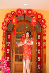 An Asian woman in traditional Chinese dress stands greeting with a happy smile during the Chinese New Year festival.