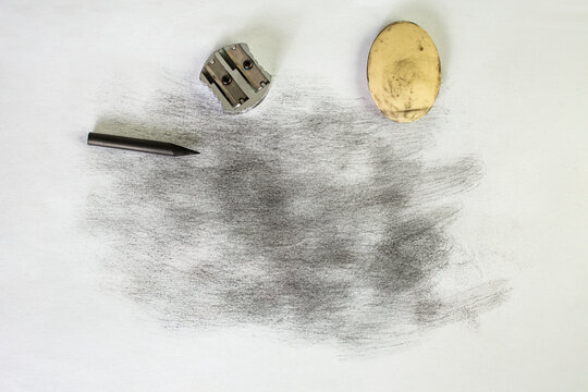 Black dust or charcoal and smudges on white paper next to a piece of graphite, an eraser and a pencil sharpener