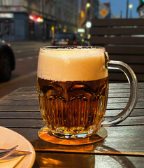 A mug of beer with foam against a blurred background of an evening city