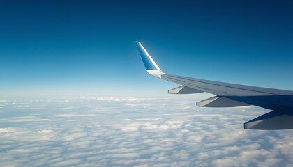 Fototapeta premium Airplane wing soaring through clear blue sky above fluffy white clouds