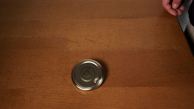Person's hands spinning a metal lid on a wooden table