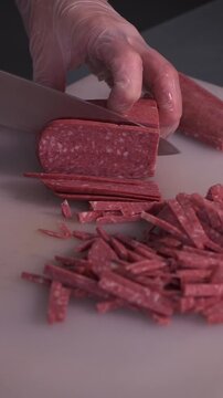 The cook cuts the sausage for the salad. Preparation of appetizers and salads