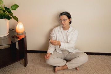 Fototapeta premium Young caucasian female meditating indoors with incense and salt lamp