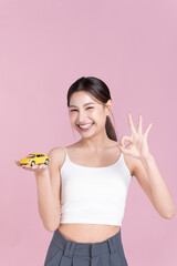 Smiling young woman holding dream car model for financial planning and car loan advertising on pink Background.
