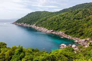 Lighthouse Bay in Koh Tao, Thailand, featuring turquoise water and green coastal landscape. Rocky shoreline with lush tropical vegetation. Scenic view of the ocean from the island.