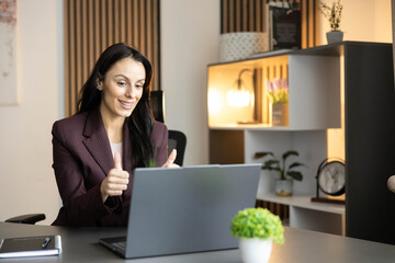 A smiling woman conveys enthusiasm and connection while interacting via laptop in her home office.