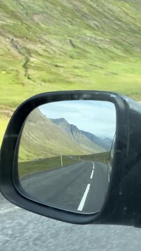 View of a side driver's rear view mirror with scenic road Icland view in the mirror itself 