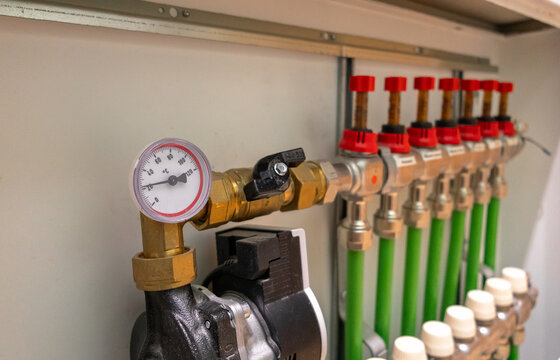 A modern domestic hydronic underfloor heating manifold with pipes, valves, flow meters, and a circulation pump. Focus on plumbing, installation, heating systems, energy efficiency, home improvement