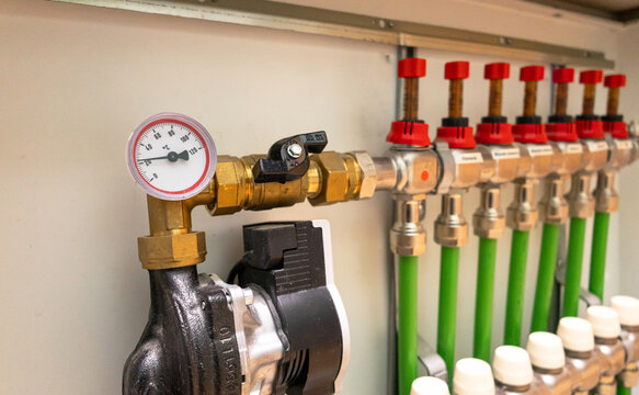 A modern domestic hydronic underfloor heating manifold with pipes, valves, flow meters, and a circulation pump. Focus on plumbing, installation, heating systems, energy efficiency, home improvement