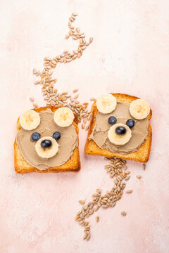 Toast displays bear faces made with banana slices and blueberries, arranged on a light background in a kitchen setting