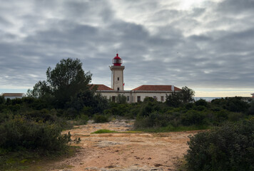 Alfanzina Lighthouse with red lantern tower rising above green coastal vegetation and rocky landscape.