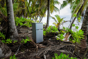Abandoned refrigerator on tropical beach under palm trees