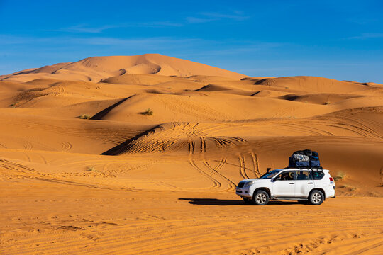 Urlaub in Marokko, in der Sahara, W&uuml;ste Erg Chebbi bei Erfoud: Faszinierende D&uuml;nenlandschaft mit einem Auto, Vierrad Gel&auml;ndewagen mit Gep&auml;ck auf dem Dach