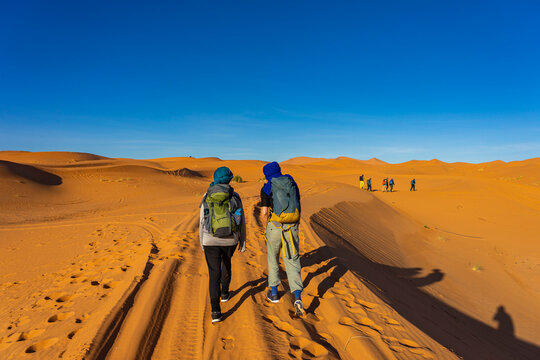 Urlaub in Marokko, in der Sahara, W&uuml;ste Erg Chebbi bei Erfoud: Faszinierende D&uuml;nenlandschaft mit zwei Frauen die Wandern mit Rucksack
