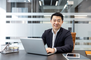 Fototapeta premium Asian businessman working on his laptop while sitting at a desk in a contemporary office setting, portraying professionalism, success, and digital business operations