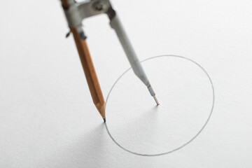 Closeup of drafting compass drawing circle on white paper background.