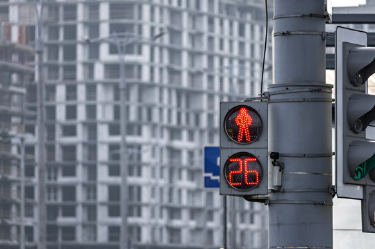 Red pedestrian traffic light with digital countdown against the background of a modern building under construction.