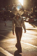 Stylish person with a disco ball head walking on a city street during golden hour sunset.