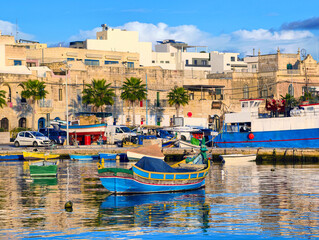 Marsaxlokk, Malta &ndash; Traditional fishing village with colorful boats, palm trees, and historic buildings at the sunny harbor. Shows authentic island life and maritime culture in Malta