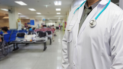 Close up of male doctor in white uniform with stethoscope standing at hospital hallway. Professional physician ready for service with blurred patients background.