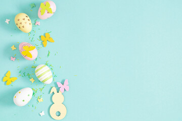 Flat lay Easter composition: decorative eggs, paper butterflies, and a bunny on a light blue background. Spring festive Easter decoration.