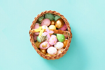 Easter eggs in a wicker basket on a turquoise background. Top view. Festive Easter decor with gold accents. Bright and stylish composition.