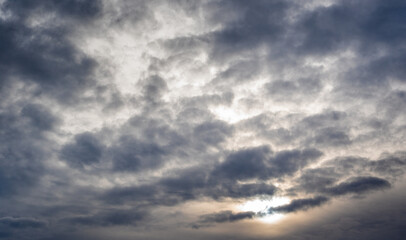 Dramatic cloud formation with varying shades of gray and hints of sunlight peeking through, creating a textured sky during twilight hours