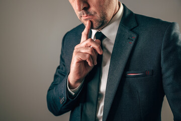 Businessman in dark suit resting index finger thoughtfully on chin with serious gaze.
