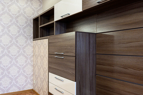 Dark wood-finish wall unit with cream drawers and open shelves; paired with light patterned wallpaper, featuring sleek metal handles.