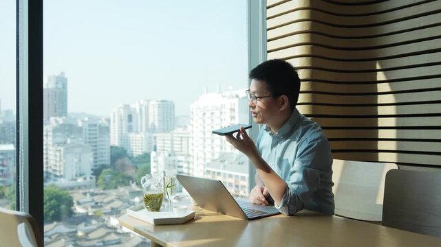 Young man using laptop computer for voice input by the window in a modern office