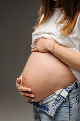 A pregnant woman gently holds her rounded belly in her hands. A warm and touching moment