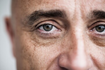 Fototapeta premium Middle-aged man with shaved head and expressive eyes, showcasing facial features and skin texture in a close-up portrait against a neutral background