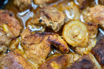 Close-up of roasted pork pieces with caramelized onion in rich meat juices. Traditional homemade dish, rustic comfort food prepared in a baking tray.